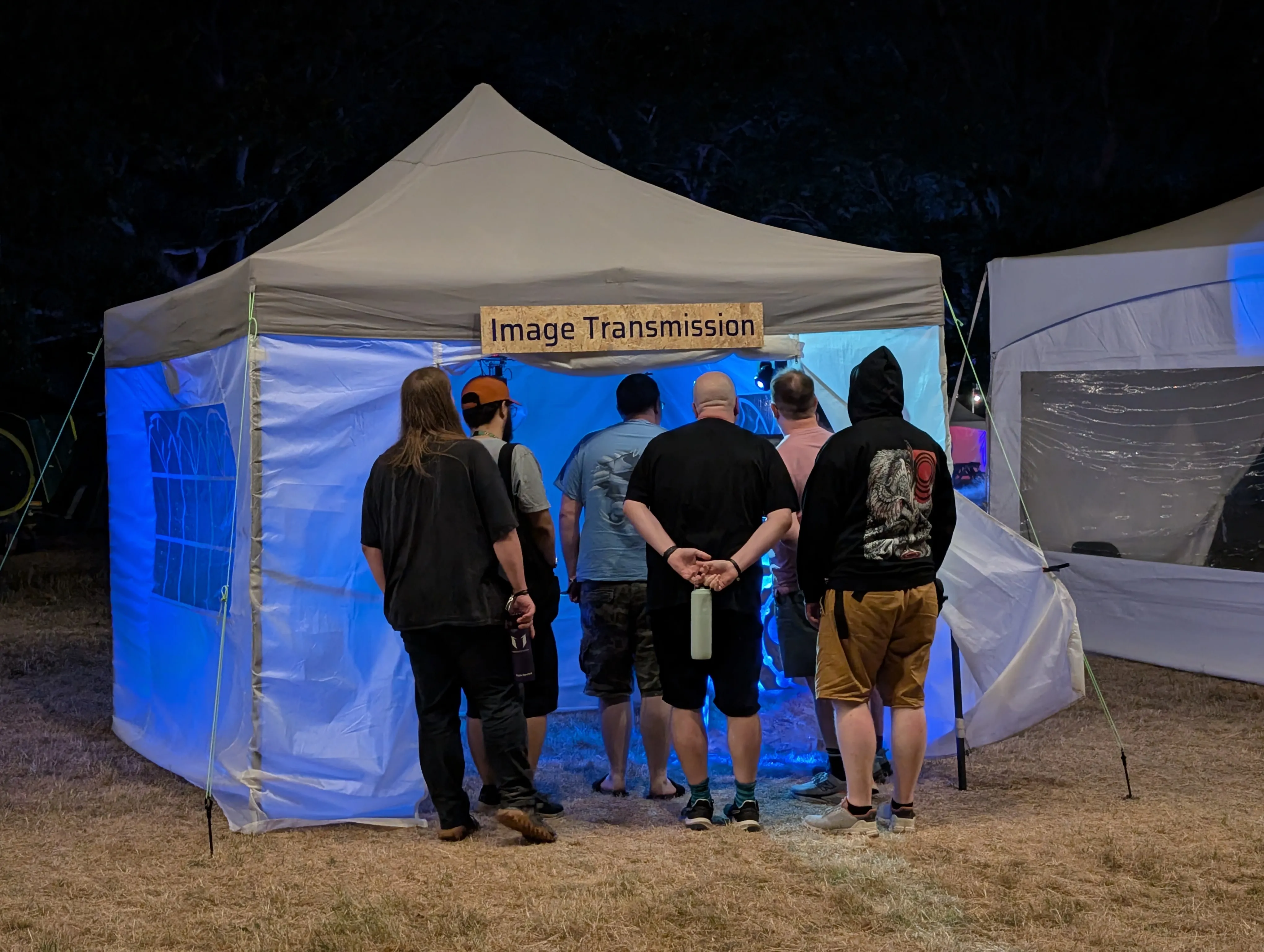A crowd gathered at the mouth of the gazebo at night, watching the installation.