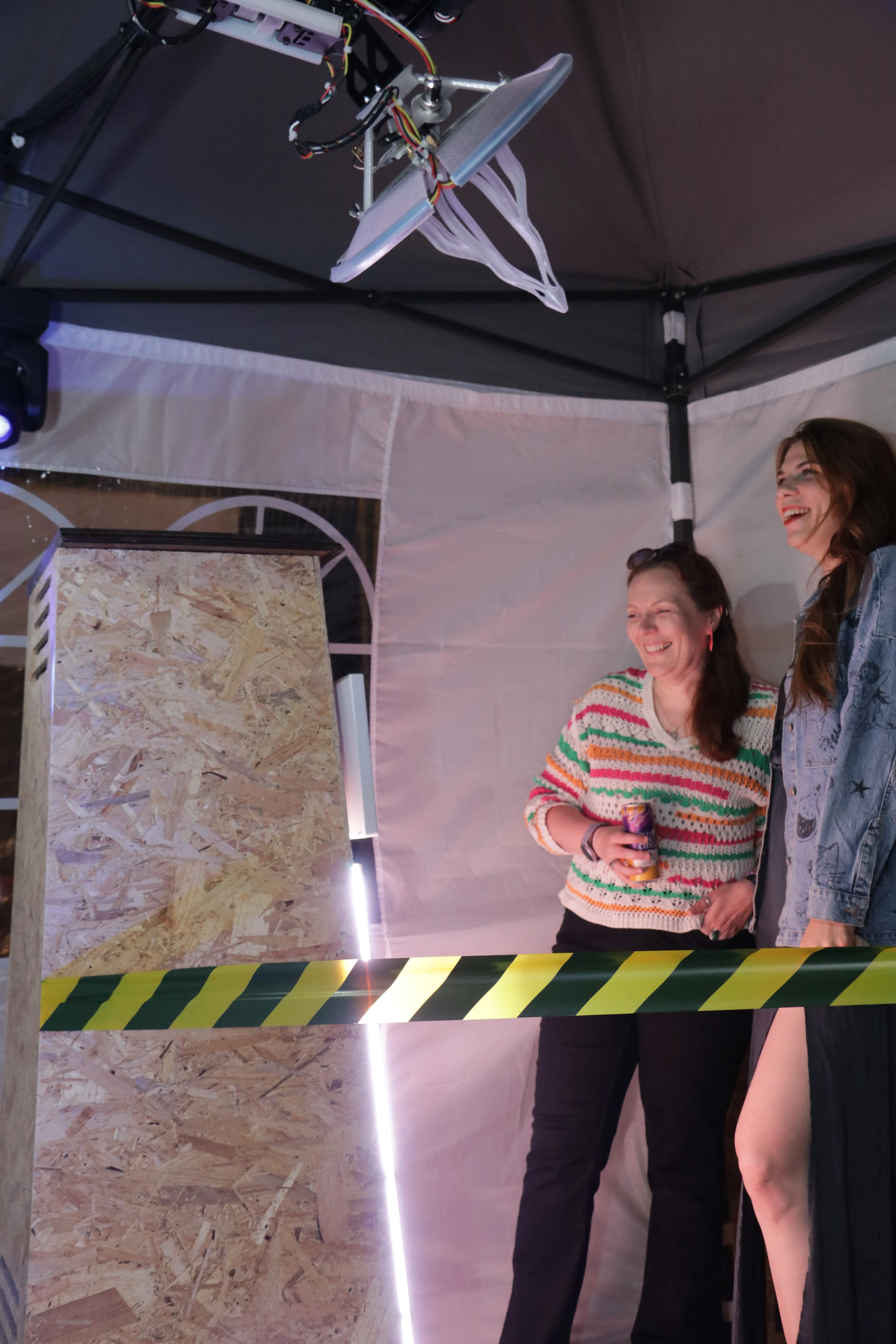 Two visitors at the booth at night, lit purple, with the arm and antenna overhead.